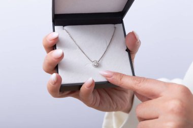 Elmas kolyeli hediye kutusunu tutan zarif manikürlü kadın elleri. Lüks, mücevher, zarif bir hediye.