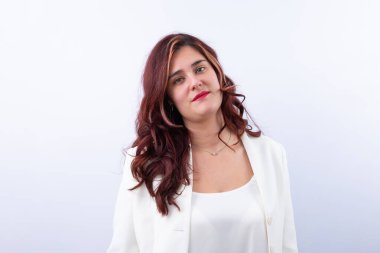 Uzun kıvırcık saçlı, beyaz takım elbiseli ve kırmızı dudaklı bir kadın kameraya rahatça bakıyor. Tarafsız arka plan, zarif ve profesyonel tarz. Uzayı kopyala Markalaşma, iş ve güven için ideal. Güçlendirme ve tarz kavramı