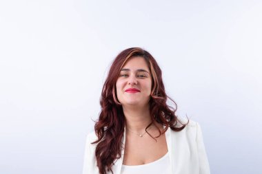 30 yaşında, uzun kızıl saçlı, kırmızı dudaklı, beyaz takım elbiseli ve elmas kolyeli, kameraya mutlu bir şekilde gülümseyen bir kadın. Tarafsız arkaplan ve kopyalama alanı. Kadın kavramı, neşe, güven ve güç.