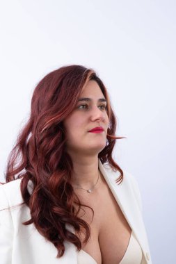 Beyaz spor ceket ve bej sutyen giyen, kırmızı dudaklı, dalgalı kızıl saçlı bir kadının portresi. Kendine güvenen ifade ve yan bakış. Uzayı kopyala Güven, zarafet ve güç kavramı.
