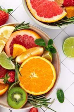 Beyaz fayanslı arka planda kaselerde canlı meyve kompozisyonu. Portakal, greyfurt, limon, limon, çilek ve kivi. Parlak renkler ve tazelik. Yaz kavramı, tazelik ve sağlıklı yaşam tarzı.