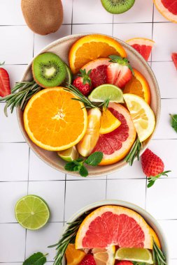 Taze meyvelerin parlak kompozisyonu: narenciye, kivi ve minimalist bir arka planda bir kasede çilek. Sağlıklı ve taze stil. Doğal besin ve canlılık kavramı