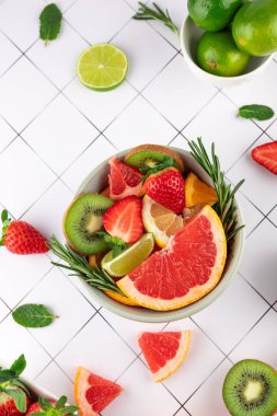 Renkli taze meyve karışımının üst görüntüsü: greyfurt, kivi, ıhlamur, limon, portakal ve beyaz ızgara arka planda bir kasede çilek. Uzayı kopyala Tazelik ve sağlıklı yaşam kavramı