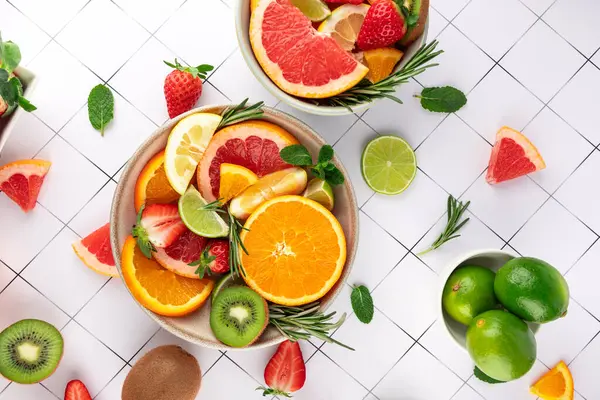 Renkli bir kase taze narenciye ve beyaz fayanslı naneli ve biberiyeli tropikal meyveler. Yaz titreşimleri. Tazelik ve sağlıklı yaşam tarzı kavramı