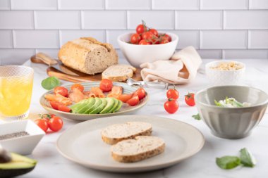 Ekmek, avokado, kiraz domatesleri, fındık, süzme peynir kasesi ve turuncu kombu çayı bardağı. Sağlıklı kahvaltı ve dengeli yemek kavramı