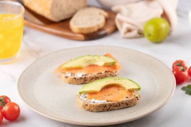 Somon, avokado ve krem peynirli tohum ekmeği minimalist bir tabakta servis edilir. Besleyici ve doğal bir kahvaltı. Sağlıklı gıda kavramı