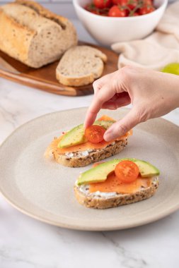 Bir kadının eli füme somon, avokado ve domatesle kadeh kaldırırken. Taze sağlıklı atıştırmalık. Sağlıklı yaşam ve temiz yemek kavramı