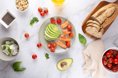 Avokado, tütsülenmiş somon ve taze malzemelerle çevrili kiraz domatesli sağlıklı bir tabağın üst görüntüsü. Sağlıklı beslenme ve dengeli beslenme kavramı
