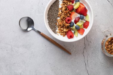 Kefir, meyve, chia tohumu ve granola, metal ve ahşap kaşık ve arkaplanda granola olan cam kavanozun üst görüntüsü. Sağlıklı sabah rutini ve doğal minimalizm kavramı