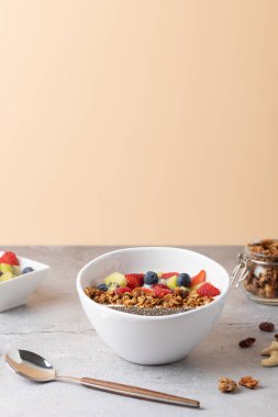 Kefir kasesi granola, chia tohumu, ahududu, yabanmersini ve kivi dilimleri. Yumuşak şeftali arkaplanı ve nötr taş yüzeyi olan parlak ve minimalist bir ortam. Arka planda küçük bir kase ve cam kavanoz var. Sağlıklı kahvaltı kavramı 