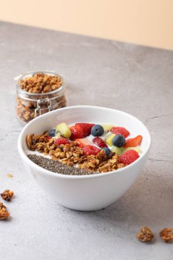Kefir, çilek, yabanmersini, ahududu, kivi, granola ve chia çekirdekli hafif taş yüzeyde. Arka planda granola kavanozu var. Sağlıklı ve doğal kahvaltı kavramı