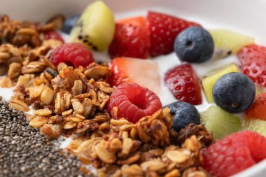 Beyaz bir kase içinde taze meyve, granola ve chia tohumları yakın plan. Canlı renkler ve çıtır çıtır dokular. Doğal gıda, enerji ve canlılık kavramı