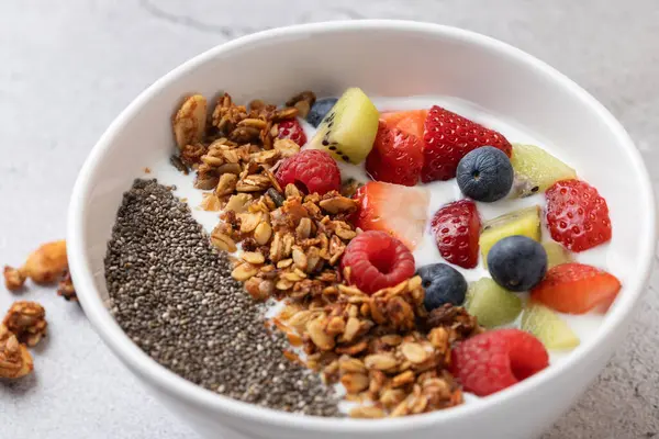 Kefir, çilek, yaban mersini, ahududu, kivi, gevrek ve chia tohumlu beyaz kâse manzarası. Açık gri arka plan. Dengeli beslenme ve sağlıklı yaşam tarzı kavramı
