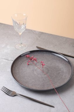 Koyu gri seramik plakalı minimalist kompozisyon ve içinde pembe bir çiçek sapı var. Yanında, kristal bir cam ve hafif beton yüzeyde modern çatal bıçak takımı var. Uzayı kopyala Zarif sofra takımı ve asgari çiçek tasarımı kavramı