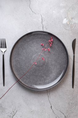Zarif ve minimalist bir kompozisyonu olan bir masanın yukarıdan görünüşü. Üzerinde modern çatal bıçak takımı ve beton bir yüzey üzerinde cam bardak bulunan biçimlendirilmiş pembe çiçekli gri bir seramik tabak. Uzayı kopyala Rafine masa estetiği kavramı 