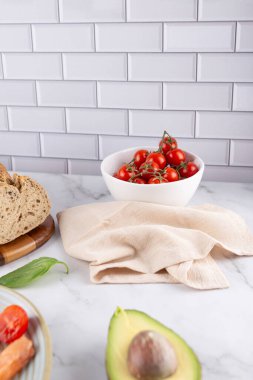 Beyaz kasede taze kiraz domatesleri, beyaz fayans zemininde tam tahıllı ekmek ve bej peçete. Basit ve doğal bir mutfak. Sağlıklı beslenme ve ev yapımı yemek kavramı