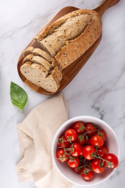 Tahtadaki tahıllı ekmeğin en üst görüntüsü. Kiraz domatesleri ve açık mermer arka planda fesleğen. Sağlıklı ve Akdeniz yemekleri. Sağlıklı kahvaltı ve doğal yaşam tarzı kavramı