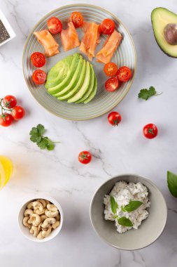 Somon, avokado ve vişneli domatesli, mermer kaplama, ricotta ve fındıklı sağlıklı kahvaltı. Üst Manzara. Temiz yemek ve doğal ev yemeği kavramı
