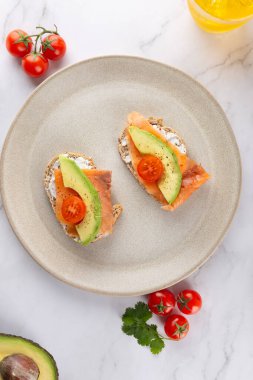 Avokado, somon ve vişneli domates tostlu kahvaltı seramik tabakta mermer yüzeyde. Uzayı kopyala Dengeli yeme ve sağlıklı yaşam tarzı kavramı