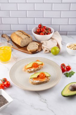 Avokado, somon ve kiraz domatesli kahvaltı bej seramik tabakta, arka planda ekmek, limon ve içecek ile. Mermer yüzey. Sağlıklı beslenme ve doğal yaşam tarzı kavramı