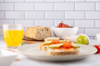 Avokado, somon ve kiraz domatesli tostlar mermer bir yüzeyde, arkada içecek ve ekmek var. Parlak bir görüntü ve doğal bir görünüm. Besleyici kahvaltı ve dikkatli yaşam kavramı