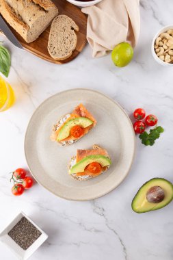 Avokado, somon ve vişne domatesli iki tostlu bir tabağın üst görüntüsü. Çevredeki malzemeler: ekmek, avokado, limon ve chia tohumları. Uzayı kopyala Sağlıklı beslenme ve taze yemek kavramı