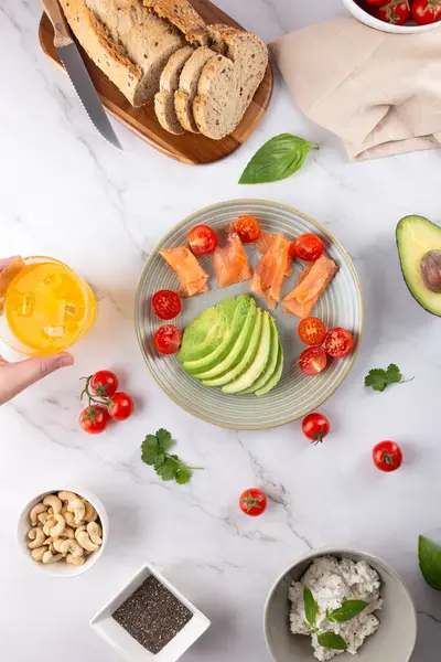 Avokado, somon ve vişneli domates, tam tahıllı ekmek ve kaju. Erkek el, bir bardak turuncu kombu çayı tutuyor. Sağlıklı gıda ve dengeli yaşam tarzı kavramı