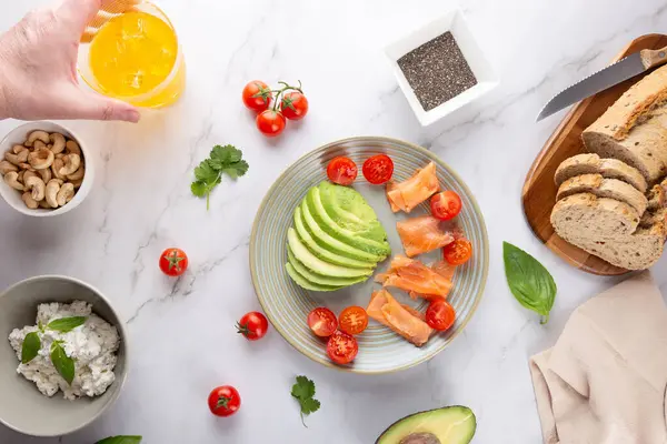 Avokado, somon, tam tahıllı ekmek, ricotta, fındık ve bir adamın elinde bir bardak kombu çayı ile besleyici bir kahvaltı manzarası. Sağlıklı beslenme ve ev yapımı mutfak kavramı