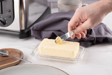 Erkek el, tereyağını mermer tezgahın üstünde bıçakla alıyor gri bir bez ve paslanmaz çelik bir tost makinesinin yanında. Yumuşak ve doğal aile sahnesi. Ev yapımı ve basit sabah rutini kavramı