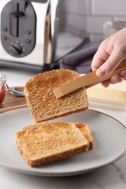Taze kızarmış ekmek ahşap maşayla toplanıyor. Ön sahne servis jestine odaklanıyor. Sağlıklı ve doğal sabah rutini kavramı