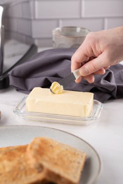 Erkek el tereyağını bıçakla kepçeleyen ve ön planda tost dilimleri olan yakın plan bir fotoğraf. Kumaş ve mutfak detaylarıyla yumuşak bir arka plan. Ev yapımı ve sağlıklı kahvaltı kavramı