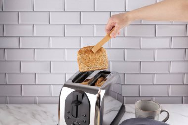 Mutfakta krom tost makinesi ve bardakla bütün buğday ekmeğini ahşap maşayla kaldıran bir kadının ön görüntüsü. Uzayı kopyala Ev yapımı kahvaltı ve sabah rutini kavramı