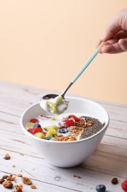 Kremalı kefir, çilek, kivi, granola ve chia ile kahvaltı kasesi bir erkeğin elinde bir kaşık kefir ve kivi ile birlikte. Pastel arka plan ve ahşap masa. Uzayı kopyala Sağlıklı gıda ve günlük sağlık kavramı
