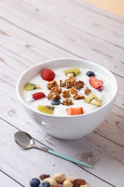 Kırsal arka planda metal kaşığın yanında çeşitli meyveler, tahıl gevreği ve fındıklı Kefir kasesi. Taze ve gerçekçi estetik. Uzayı kopyala Dengeli yaşam tarzı kavramı