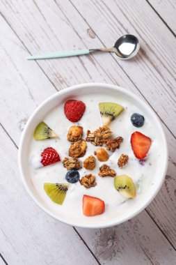 Beyaz ahşap arka planda kefir kasesi, kivi, böğürtlen ve granola ile kaşık. Minimalist tarzda. Uzayı kopyala Gerçek yemek ve dikkatli yaşam tarzı kavramı