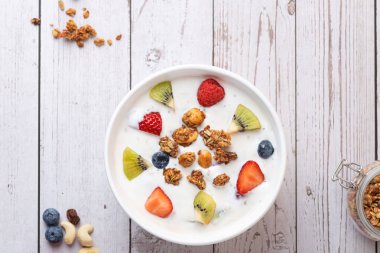 Kefir, kivi, böğürtlen ve granola içeren beyaz bir kâse. Cevizler, kuru üzümler ve yabanmersinleri kırsal alana saçılmış. Uzayı kopyala Dikkatli yeme ve sağlıklı yaşam tarzı kavramı