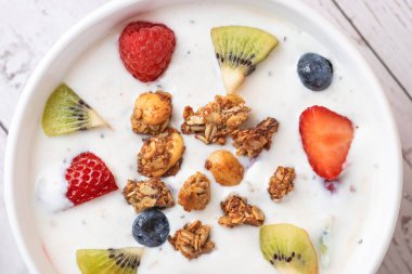 Beyaz arka planda kefir, granola, kivi, çilek, yabanmersini ve ahududu ile yakın plan beyaz kasede. Uzayı kopyala Günlük sağlıklı beslenme ve probiyotik kavramı