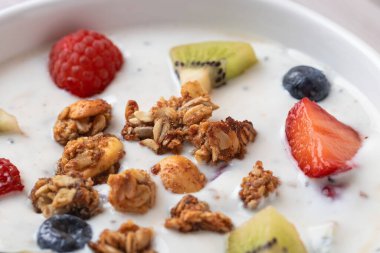 Ön yakın plan kefir, taze meyve ve beyaz kasede granola. Doğal doku ve canlı renkler. Sağlık, gerçek gıda ve probiyotik kavramı