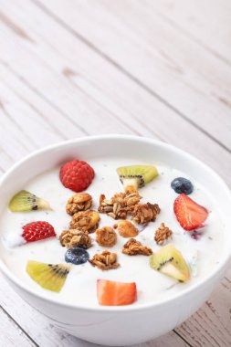 Kefir, granola ve beyaz ahşap yüzeyde renkli meyvelerle dolu tabağın dikey görüntüsü. Minimalist tarzda. Uzayı kopyala Sağlıklı ve dengeli yeme kavramı