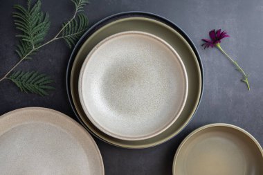 Yeşil yapraklı ve gri arka planda mor çiçekli seramik tabakaların üst görüntüsü. Sanatsal kompozisyon. Doğal estetik ve minimalist tasarım kavramı