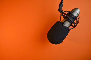 Turuncu arka planda siyah köpüklü ön camlı stüdyo mikrofonu podcast, yayın ve ses kaydı için hazır.