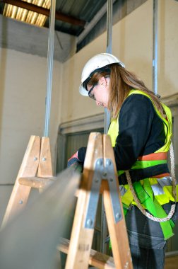 Emniyet kemeri takan kadın müteahhit inşaat sahasında çalışıyor, alçıpan takıyor.