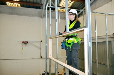 Metal iskelete alçı döşeyen, inşaat alanında güvenlik ekipmanı takan kadın işçi.