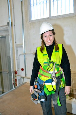 Emniyet kemeri ve kask takan kendine güvenen inşaat işçisi, aletleri tutuyor, sahada çalışmaya hazır.