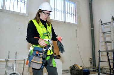 Güvenlik kaskı ve yelek giyen kadın inşaat işçisi inşaat alanında eldiven takıyor.