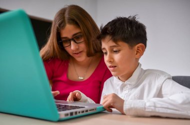 Genç öğretmen ders sırasında öğrencisine dizüstü bilgisayar kullanarak yardım ediyor.