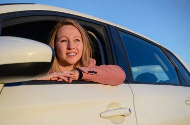 Araba camından sarkan genç iş kadını güneşli bir günde araba yolculuğunun tadını çıkarıyor.