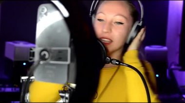 Genç bir kadın kayıt stüdyosunda profesyonel bir mikrofon kullanarak vokalleri kaydediyor.