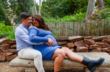 Hamile bir kadın ve kocası parkta bir bankta oturmuş bebeklerinin beklentilerinin keyfini çıkarıyorlar.