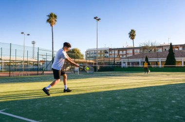 Konsantre tenisçi güneşli bir kortta forehand vuruyor